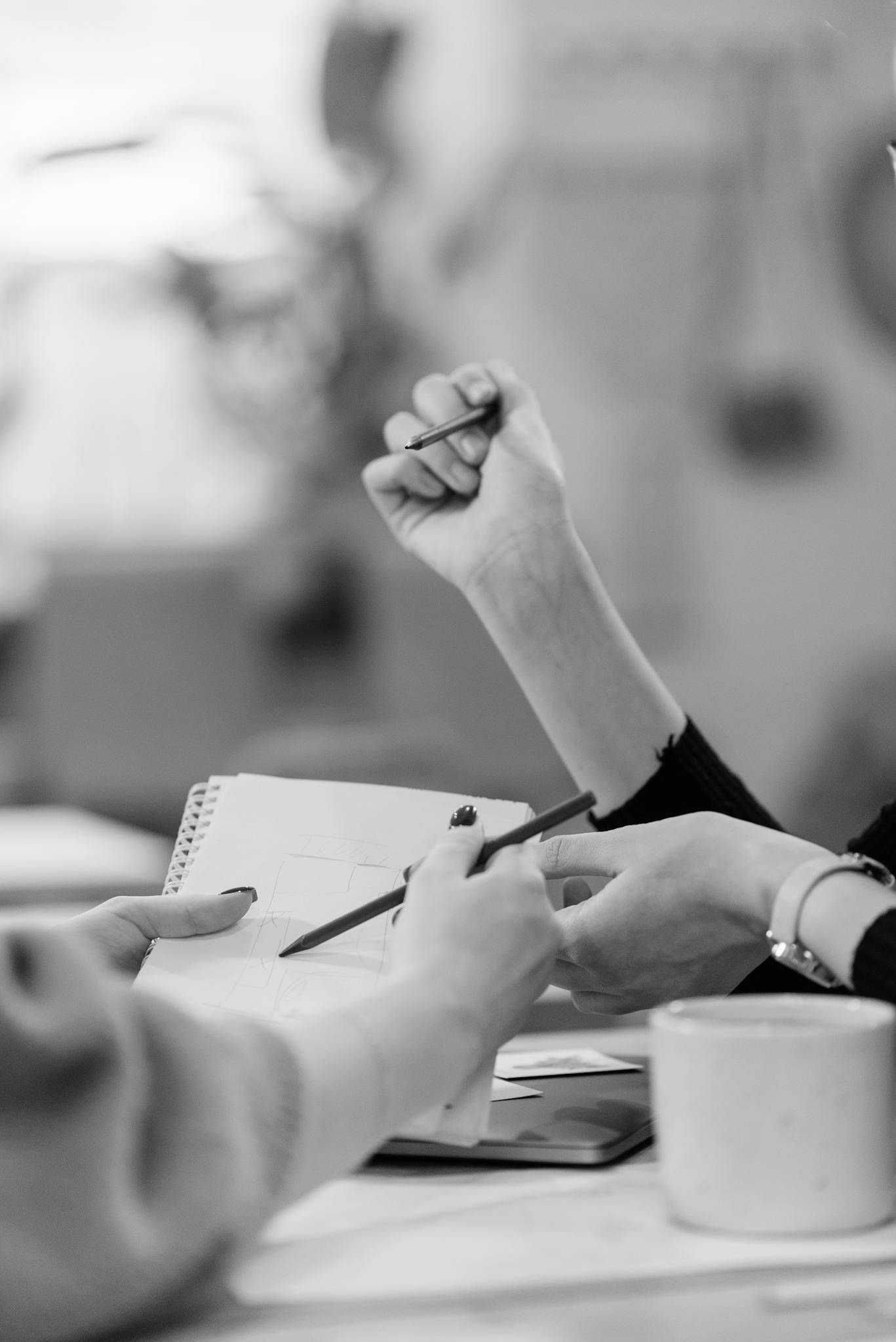 Black and white image of people collaborating at a desk, focusing on hands writing.